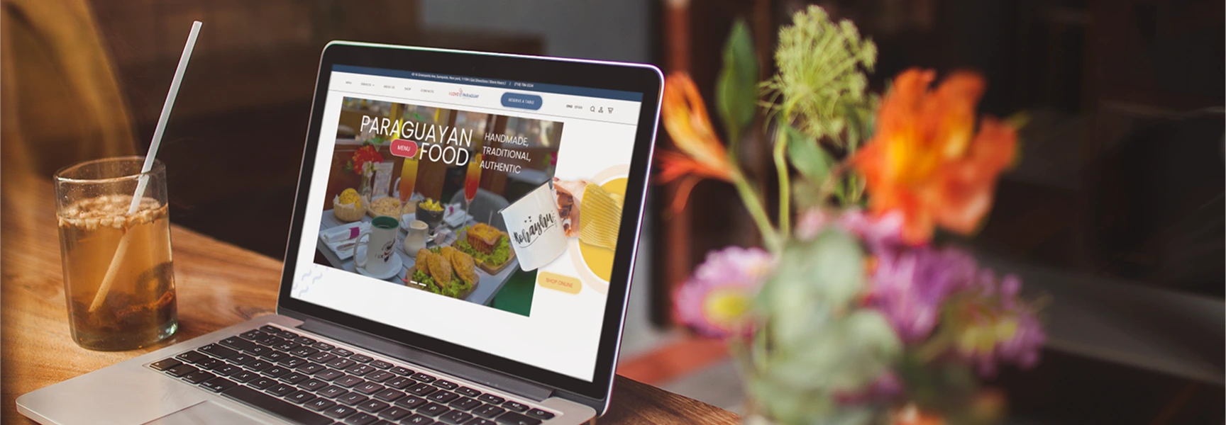 Paraguayan food website displayed on a laptop in a warm restaurant setting.